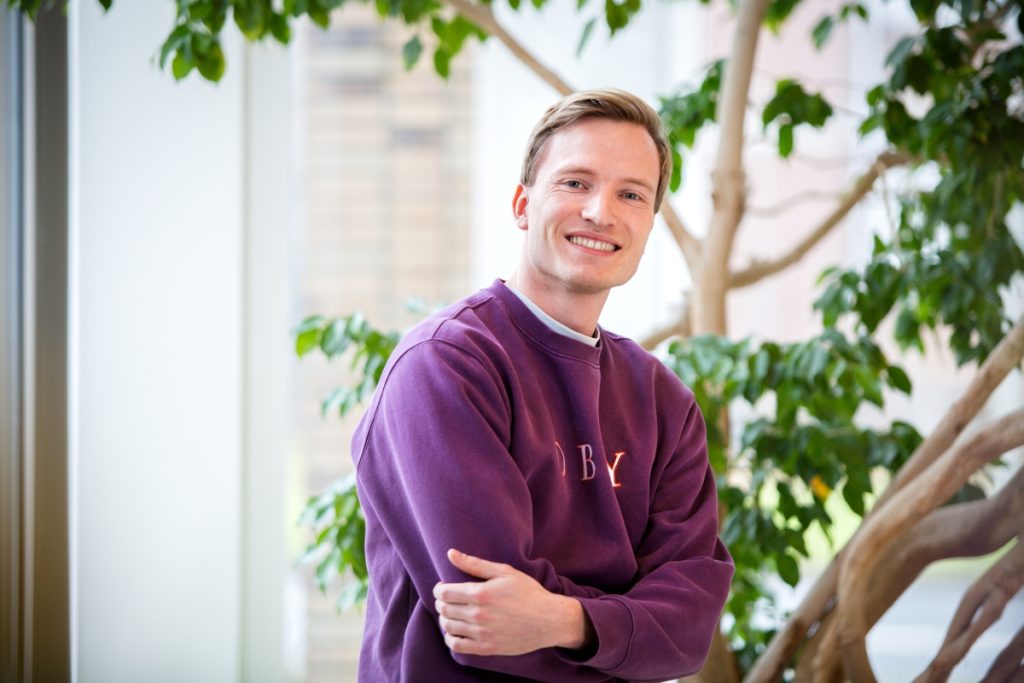 Een software engineer met een paarse trui zit in de centrale hal bij Technolution, portret 5 van 5