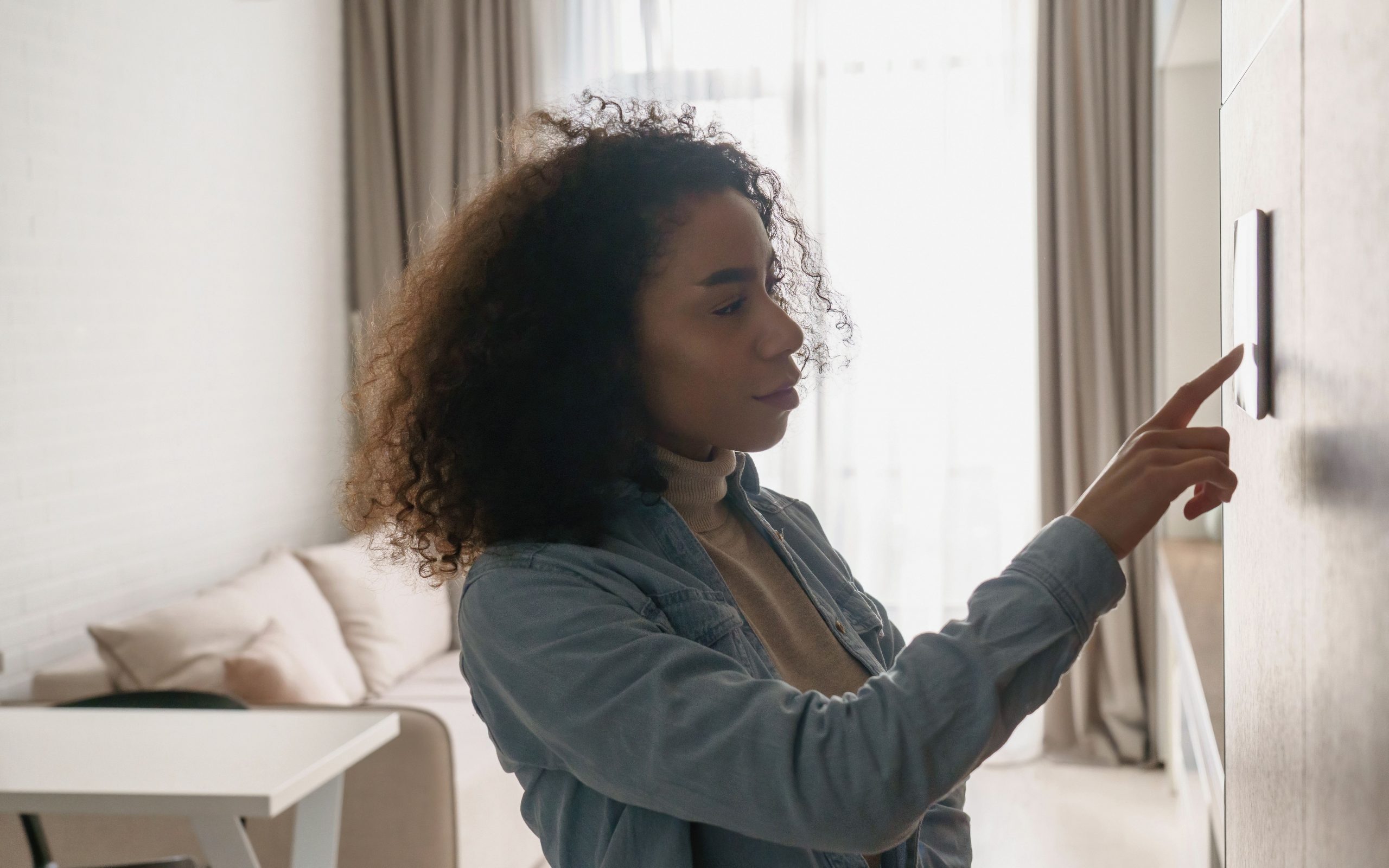 African woman using smart home touch screen technology in apartment.